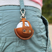 Brown leather golf ball holder attached to a belt, worn on pants, with a golf ball securely placed inside. The holder features a smooth leather texture, precise stitching, and a compact design for convenient access