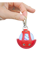 A close-up of a red leather golf ball holder with visible stitching and metallic rivets, held by a hand. The holder features a secure clip at the top and an open-front design showcasing a white golf ball inside